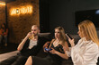 © SlavaStock - Group of friends engage in console gaming playing popular video games. Female gamer shares photo of controller via phone in social media