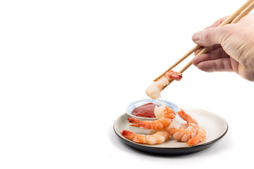 Wall Mural - A hand picking up a cooked peeled shrimp with chop sticks to dip into seafood sauce isolated on white