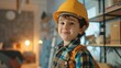Young child wearing a yellow hard hat and blue plaid shirt standing in a room with shelves and a clock smiling at the camera.