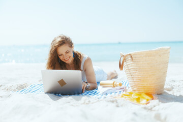 Wall Mural - smiling modern woman on ocean coast using laptop