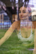 © Marino Bocelli - young cute woman in tight sports suit training on exercise bike in gym view through window reflection