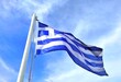 Photo of the national flag of Greece waving against a light clouded sky.