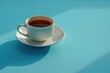 A cup of coffee on a saucer rests on a blue table. The coffee is a dark brown color and there is steam rising from the cup