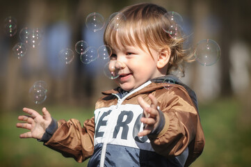 Happy smiling cute toddler delights in chasing floating soap bubbles, bathed in sunlight amidst nature. Love and family concept