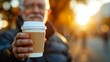 man in warm autumn clothes holds a paper cup with latte in his hands. autumn leaves on the background.
Concept: seasonal drinks and coffee to go
