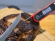 Smoked and grilled beef eye of round pulled from the heat to rest, knife ready to cut, thermometer is over 130 F