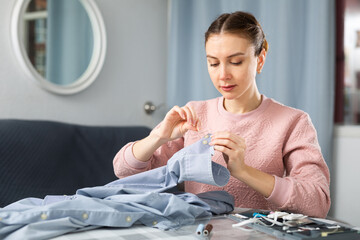 Wall Mural - Portrait of young woman housewife stitching button on shirt