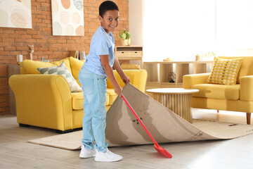 Sticker - Cute African-American boy sweeping dust under carpet with broom in living room