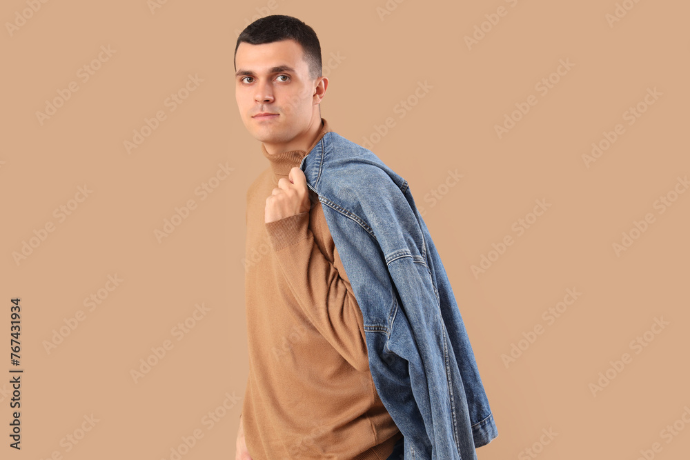 Stylish young man with denim jacket on brown background