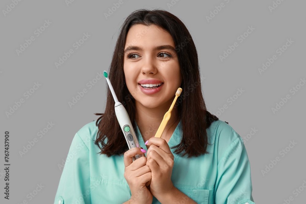 Female dentist with toothbrushes on grey background. World Dentist Day