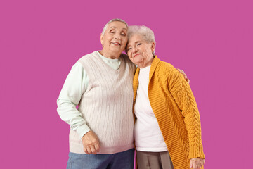 Wall Mural - Senior female friends hugging on purple background