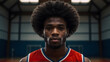 A portrait of a black young basketball player with an afro hairstyle stands on a basketball field