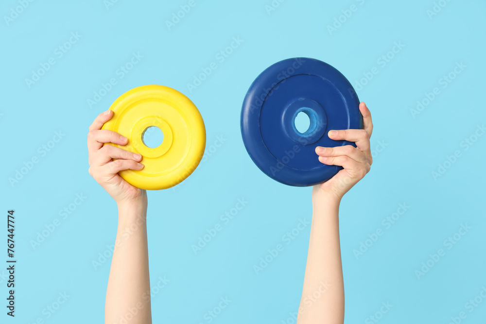 Female hands with barbell plates on color background, closeup
