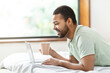 © Prostock-studio - Man lying in bed using laptop and holding cup