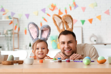 Wall Mural - Little girl with her father in Easter bunny ears hiding near table at home