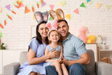 Fototapeta Dmuchawce - Happy family in Easter bunny ears sitting on sofa at home