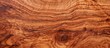 A closeup of a piece of hardwood flooring, showcasing the beautiful amber and brown tones of the wood grain pattern. The varnish highlights the peach undertones of the wood stain