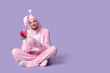 Poster - Young man in bunny costume with beautiful flowers on lilac background. Easter celebration