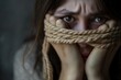 A woman holding a rope tightly around her face, expressing fear and restraint.