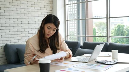 Wall Mural - Asian Female freelance using laptop at home office desk. Woman reading financial graph chart Planning analyzing marketing data. Asian female people working office firm with business stuff, coffee cup