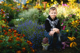 Fototapeta  - A boy sits in a garden with flowers.