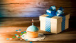 A quaint, nostalgic scene featuring a single birthday vanilla cupcake with light blue frosting topped with a single burning candle. Beside the cupcake is a gift wrapped in blue paper