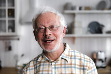 portrait of elderly cheerful man standing in cozy kitchen and smiling
