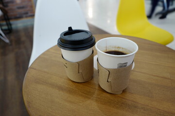 Two coffees in paper cups, one glass with a lid, on a table in a cafe