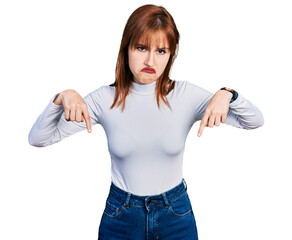 Sticker - Redhead young woman wearing casual turtleneck sweater pointing down looking sad and upset, indicating direction with fingers, unhappy and depressed.