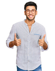 Wall Mural - Young handsome man wearing casual clothes and glasses success sign doing positive gesture with hand, thumbs up smiling and happy. cheerful expression and winner gesture.