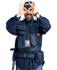 Poster - Young handsome man wearing police uniform doing ok gesture like binoculars sticking tongue out, eyes looking through fingers. crazy expression.