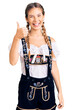 © Krakenimages.com - Beautiful caucasian woman with blonde hair wearing octoberfest traditional clothes doing happy thumbs up gesture with hand. approving expression looking at the camera showing success.