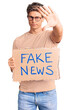 © Krakenimages.com - Young handsome man holding fake news banner with open hand doing stop sign with serious and confident expression, defense gesture