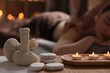 Spa therapy. Beautiful young woman lying on table during massage in salon, focus on burning candles, stones and herbal bags