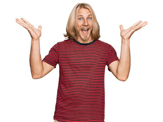 Wall Mural - Caucasian man with blond long hair wearing casual striped t shirt celebrating crazy and amazed for success with arms raised and open eyes screaming excited. winner concept