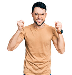 Poster - Hispanic man with beard wearing casual t shirt angry and mad raising fists frustrated and furious while shouting with anger. rage and aggressive concept.