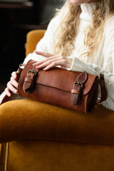 Poster - beautiful curly blond hair woman posing with a small tube brown bag in a vintage chair