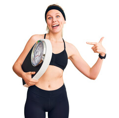 Wall Mural - Young beautiful blonde woman wearing sportswear holding weighing machine smiling happy pointing with hand and finger