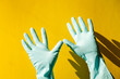 house cleaning concept. hands in blue rubber household raised up and waving on yellow background.