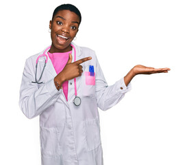 Canvas Print - Young african american woman wearing doctor uniform and stethoscope amazed and smiling to the camera while presenting with hand and pointing with finger.