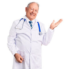 Canvas Print - Senior handsome grey-haired man wearing doctor coat and stethoscope smiling cheerful presenting and pointing with palm of hand looking at the camera.