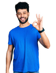 Wall Mural - Young arab man with beard wearing casual blue t shirt smiling positive doing ok sign with hand and fingers. successful expression.