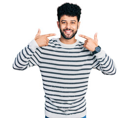 Poster - Young arab man with beard wearing casual striped sweater smiling cheerful showing and pointing with fingers teeth and mouth. dental health concept.