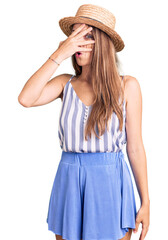 Wall Mural - Young beautiful blonde woman wearing summer hat peeking in shock covering face and eyes with hand, looking through fingers with embarrassed expression.