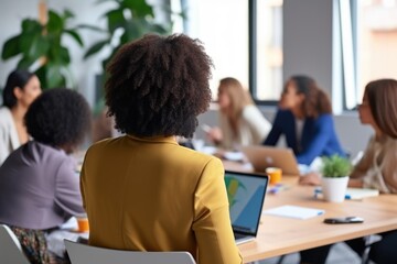 The back view of a woman attending a diverse business meeting in a bright, green office space. View of Business Meeting From Behind Participant