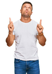 Canvas Print - Handsome muscle man wearing casual white tshirt pointing up looking sad and upset, indicating direction with fingers, unhappy and depressed.