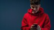 young man in a red sweatshirt smiling, using a phone on a dark blue background, professional color correction.