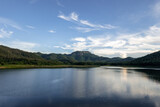 Fototapeta Natura - Serene Lake with Lush Hills Under a Blue Sky
