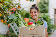 A smiling young woman carries a box of fresh organic groceries
