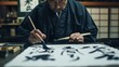 A traditional calligrapher carefully draws Japanese characters with a brush and black ink on white paper in a serene setting.